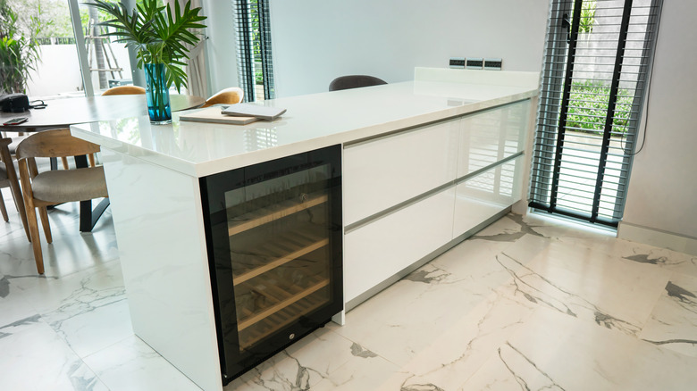 An under-counter fridge with a clear glass door is in a white kitchen.