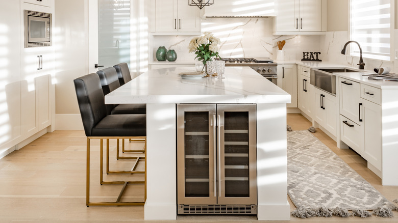 A modern kitchen has a built-in under-counter fridge with double doors and a front vent.