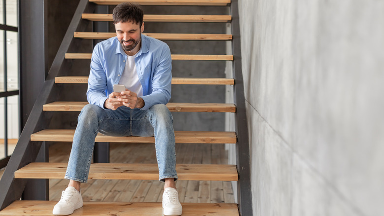 Man using his smartphone while sitting on a plain staircase in his home