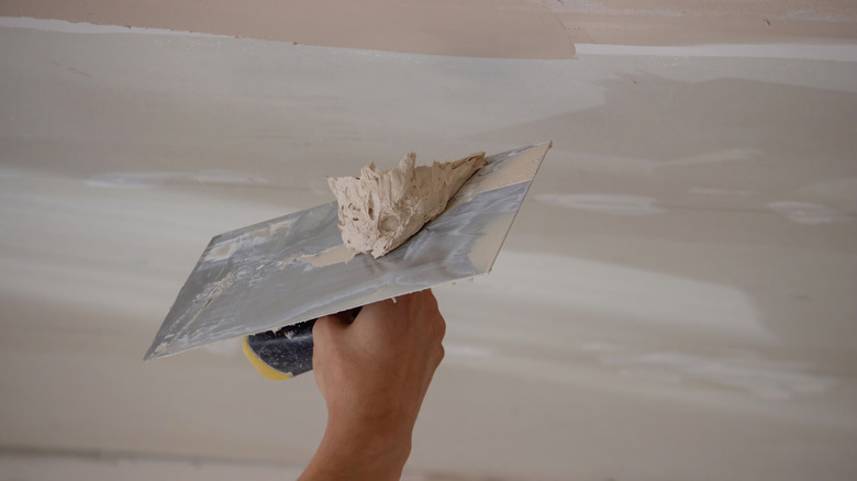 Person applying putty over ceiling repair