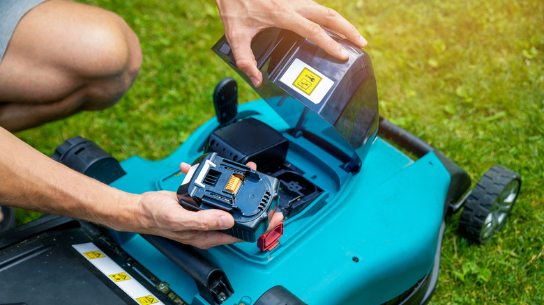 man putting battery into lawnmower