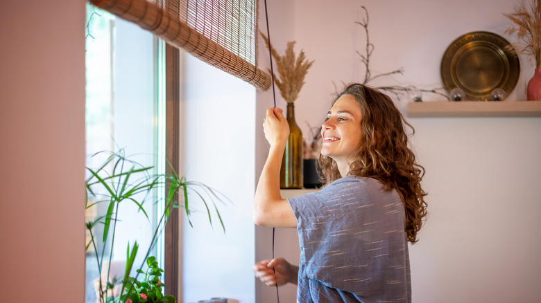 woman opening bamboo window coverings