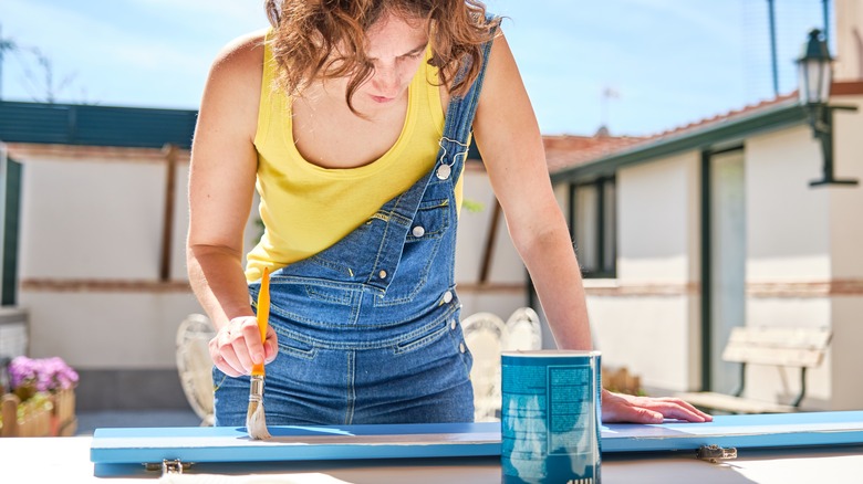 Woman in yellow shirt painting a blue cabinet door