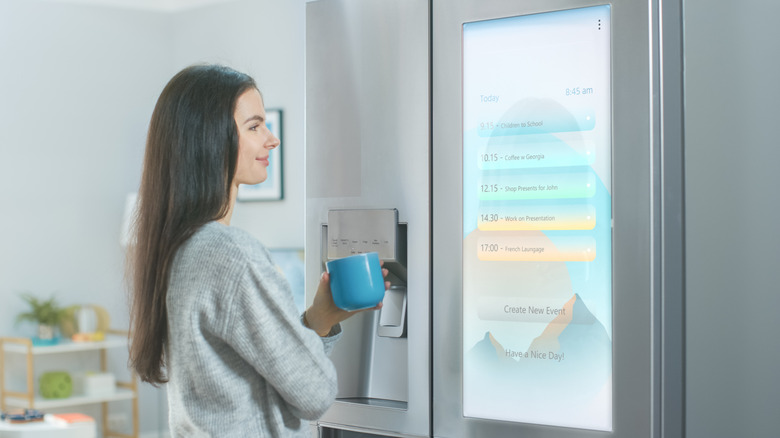 Woman holding coffee mug while reading to-do list on a smart refrigerator screen display