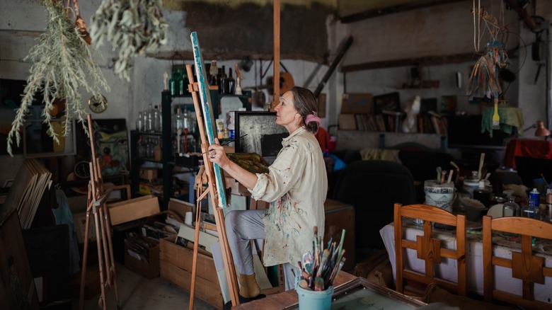 A woman looking at a canvas in a paint-strewn garage