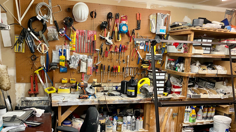 A garage workshop is cluttered with a bench, tools, bottles and cans