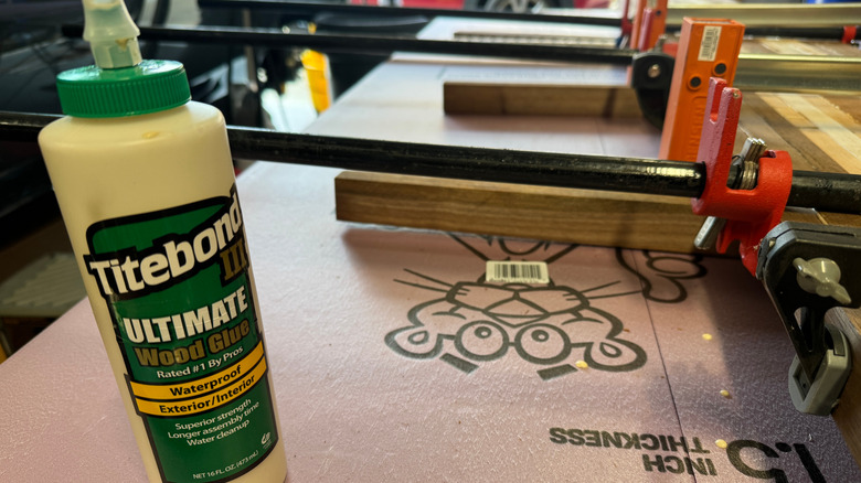 A bottle of Titebond wood glue sits on a workbench with wood in clamps behind it