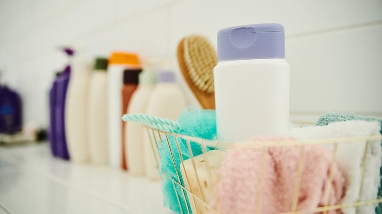 Closeup of a cluttered shower ledge with loofahs, brushes, washcloths, and bottles