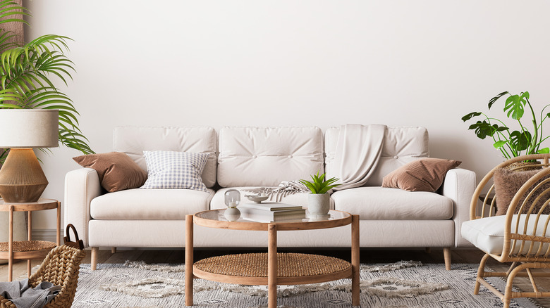 Blank white wall above white couch surrounded by plants and wooden furniture