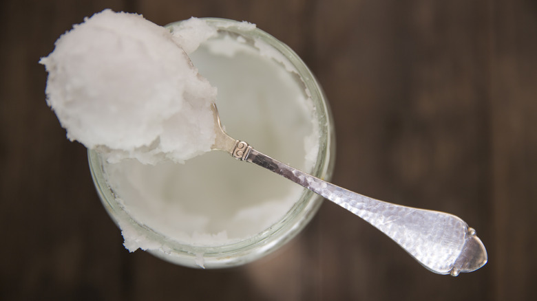 A spoon with coconut oil balancing on a jar