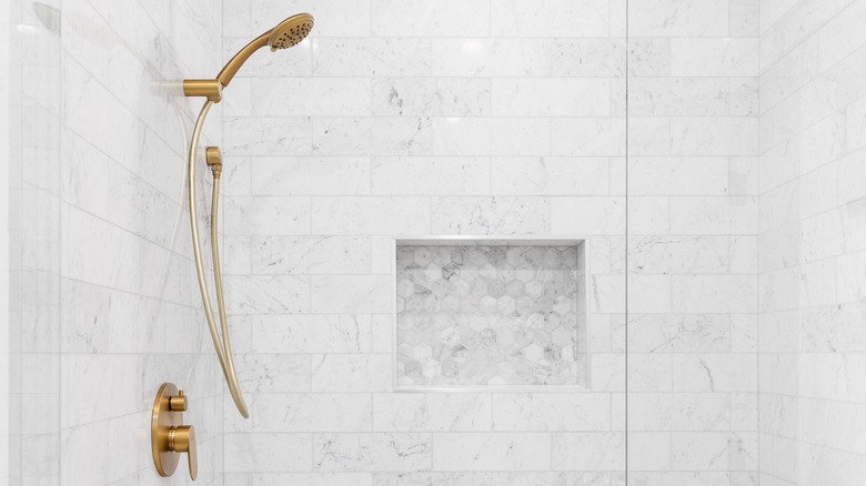 Pale tiled shower with storage niche and gold hardware