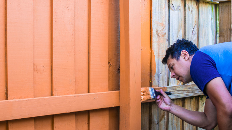 man painting fence orange