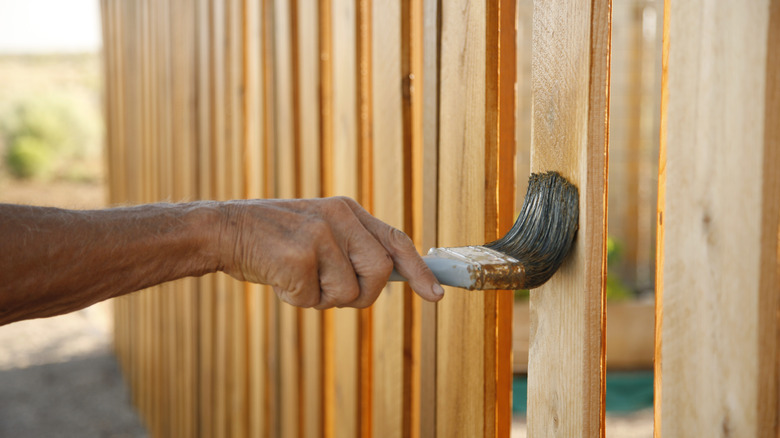 hands staining a wooden fence