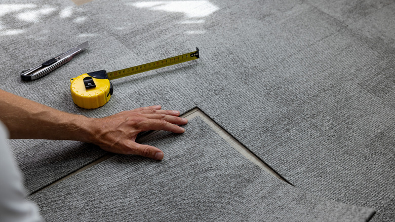 Technician installing grey carpet tiles on floor