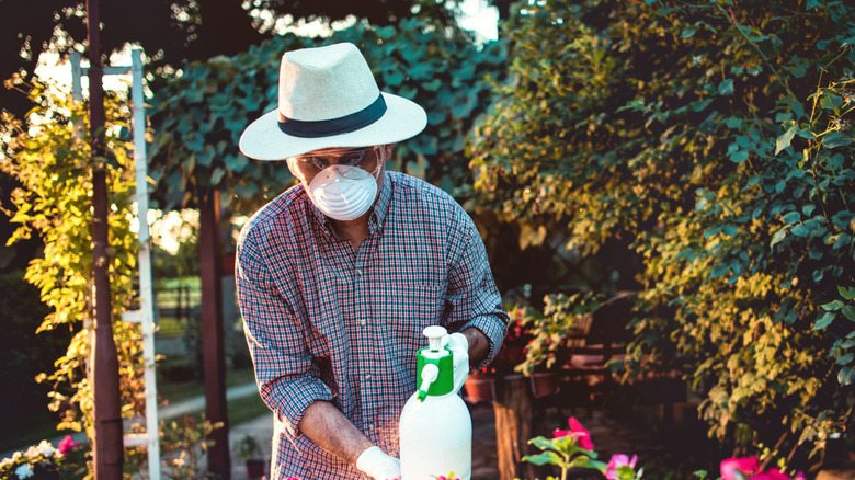 A gardener wears a mask, glasses, and other protective wear while treating the garden