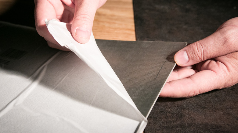 A person removing the backing of peel-and-stick tiles