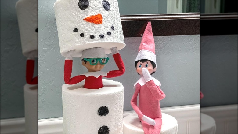 a toy elf hiding in a toilet paper snowman