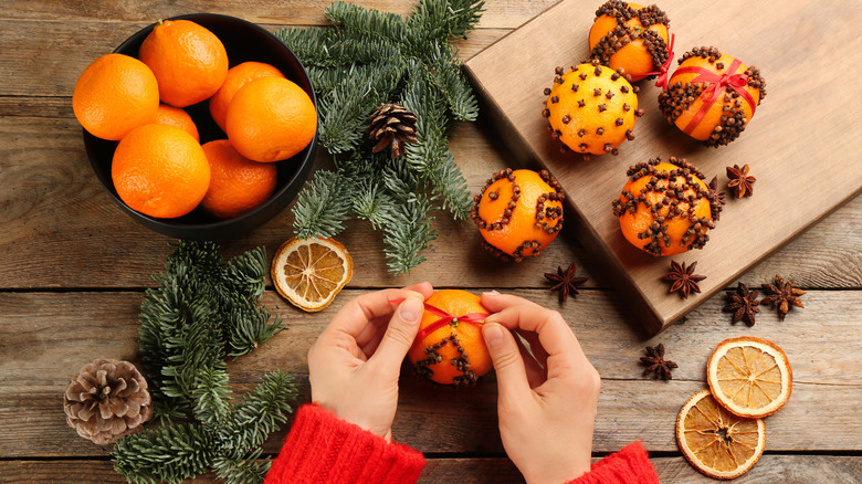 Pomander balls at wooden table and hands tying ribbon around a pomander ball