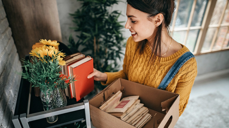 Woman putting books on crowded shelf in home