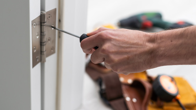 A person with a screwdriver removing door hinges