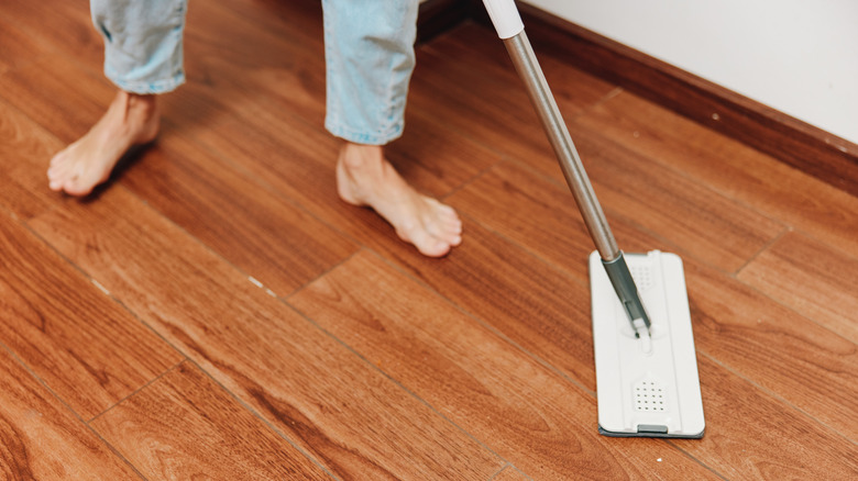 A person with bare feet and jeans applying a mop to hardwood floor