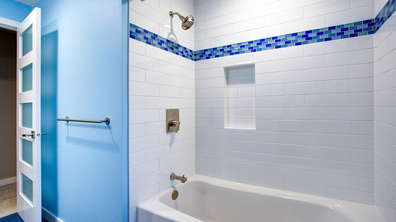 A white tiled shower with a plain white niche and decorative blue tile pattern under the shower head