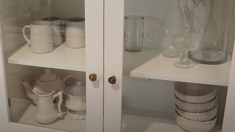 White cabinet with glass doors and white dishware inside