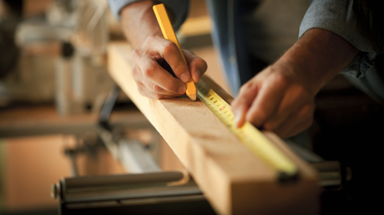 Person marking measurement on wooden plank