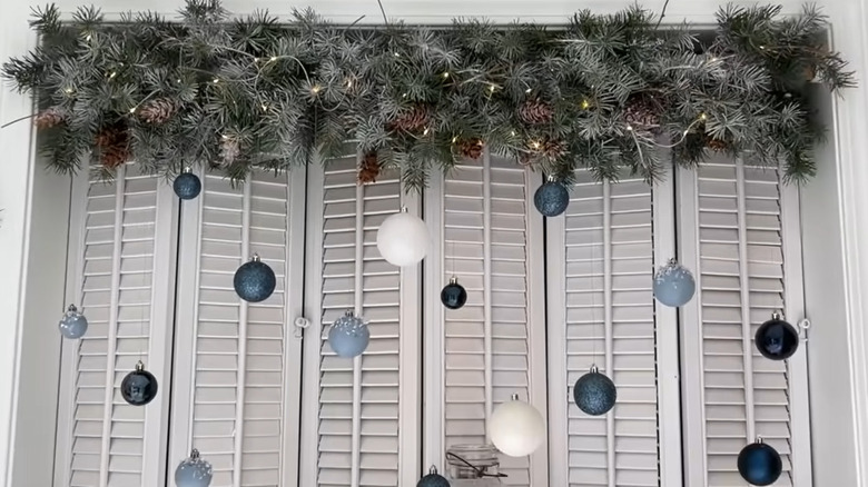 Evergreen garland hanging from window frame, strung with lights and hanging ball ornaments