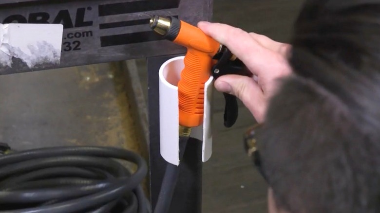 Person putting orange hose head on PVC holder mounted to metal shelf