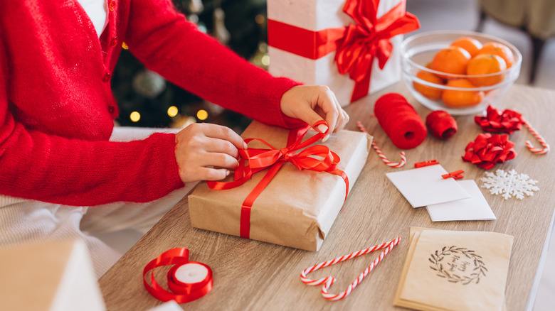 A person ties a ribbon on a wrapped Christmas present