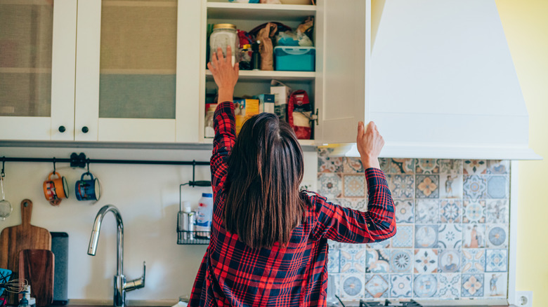 woman placing jar in kitchen cabinet