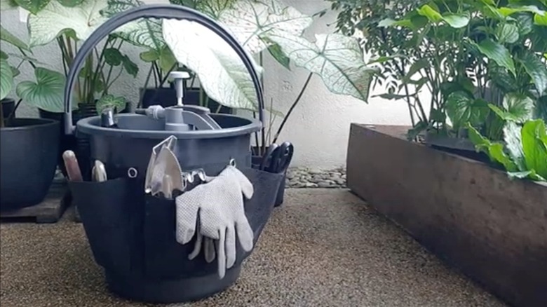 Plastic gray bucket lined with pockets holding gardening tools outside