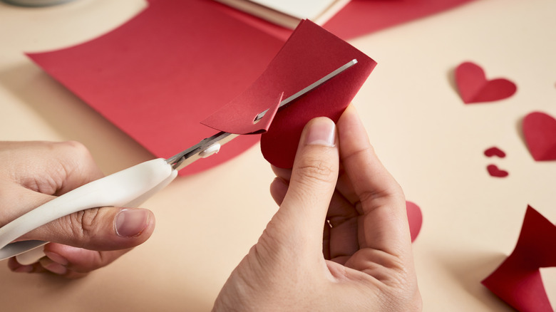 Person cutting hearts out of red paper