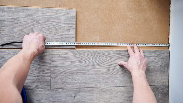 man holding a measuring tape in hand as he installs laminate boards on wall with underlayment