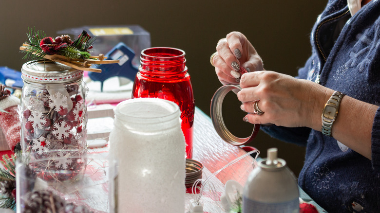 A person working on holiday crafts with various jars and supplies on the table