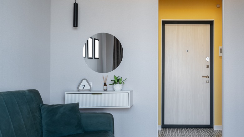 A round mirror over a white shelf near the front door