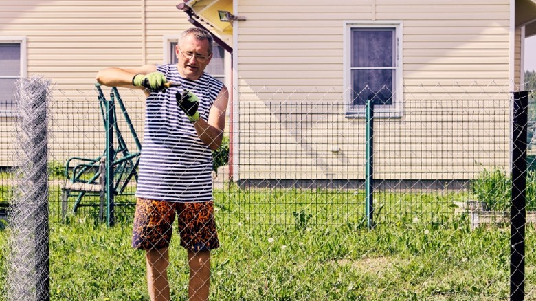 man installing metal link in yard in front of yellow vinyl-sided house