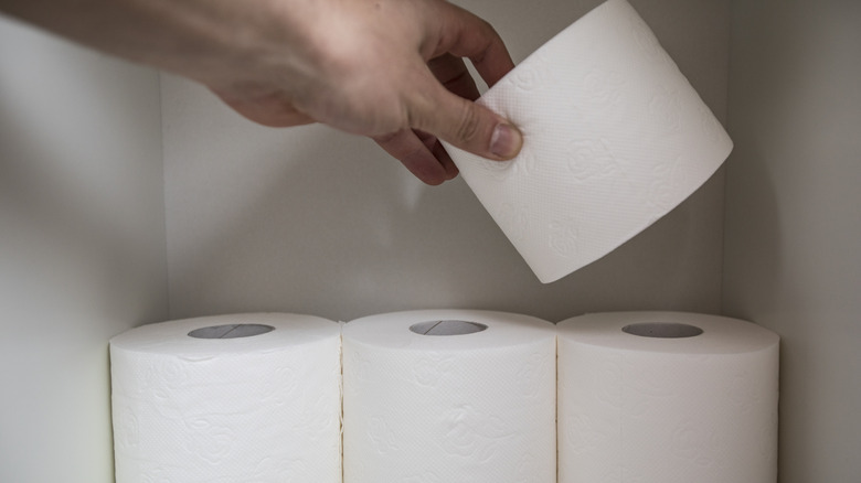 A person stores toilet paper rolls in a cabinet.