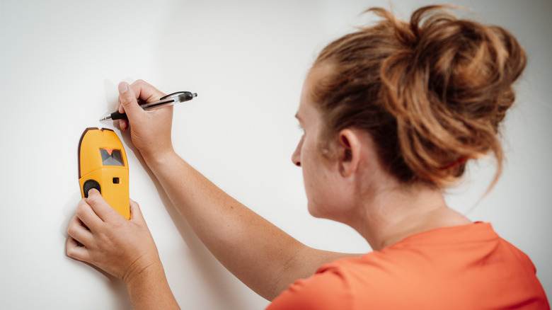 Person using a stud finder to find out where to hang shelves