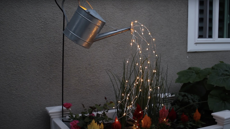 glowing watering can hung over flowers