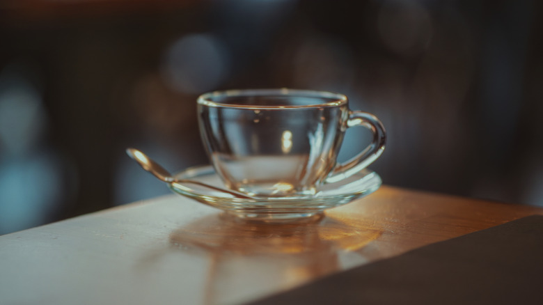 Plain glass tea cup and saucer sitting on a countertop.