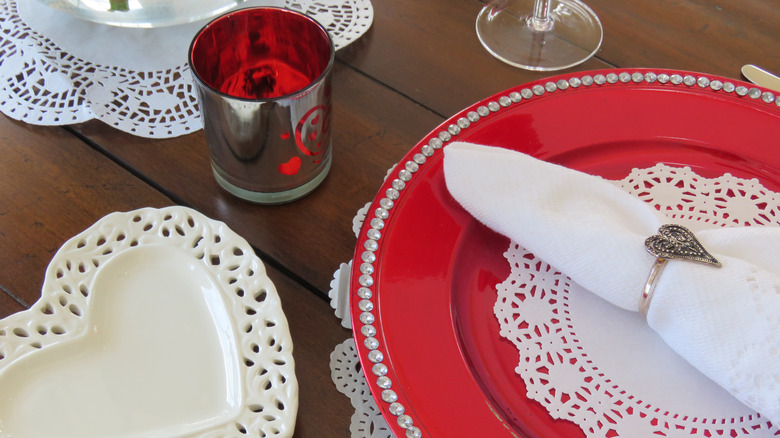 Table decorated with red plate, white heart-shaped plate, and candle for Valentine's Day