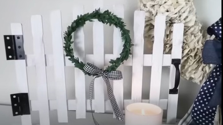 While picket fence decor piece with a wreath and candle.