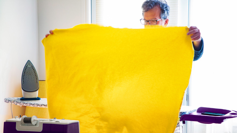 Man placing yellow blanket on ironing board