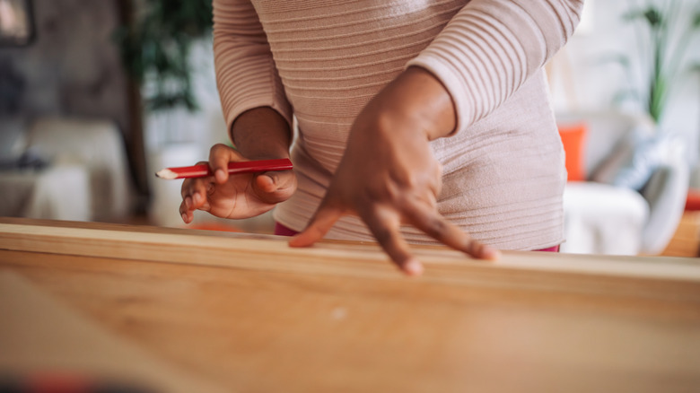 person with a pencil in hand marking wood for a project