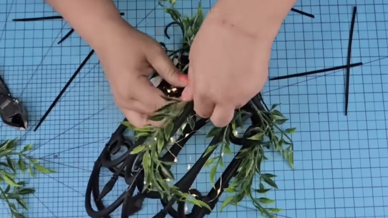 Hands are attaching faux greenery to a DIY lantern.