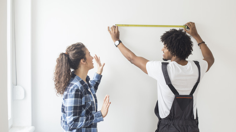 Young couple measuring the wall in their living room