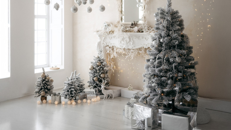 A winter wonderland scene with Christmas trees, empty fireplace, silver-wrapped gifts, and string lights