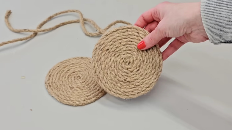 A person with painted nails holds two completed coiled jute coasters